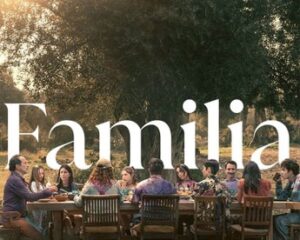 Diverse group of people seated around a long wooden table outdoors at sunset, sharing a meal, with the word 'Familia' overlaid.