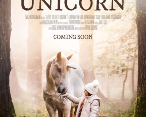 Poster for Tale of the Forest Unicorn: a child feeds a white unicorn in a sunlit forest; Coming Soon.