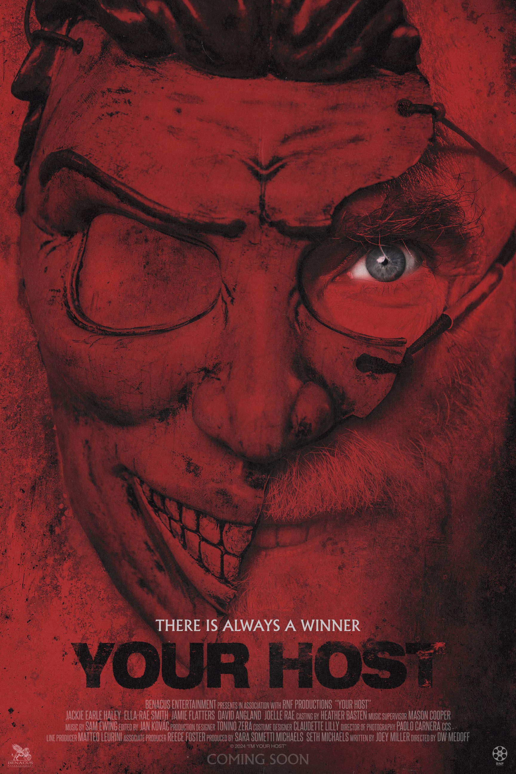 Close-up of a terrifying red-hued face with stitched grin and glasses, blue eye showing, poster for 'Your Host'.