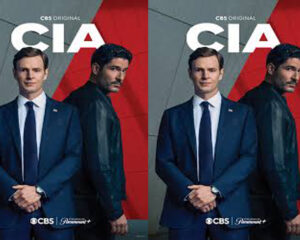 Two men in dark suits pose together against a gray and red backdrop with a CBS Original logo nearby.